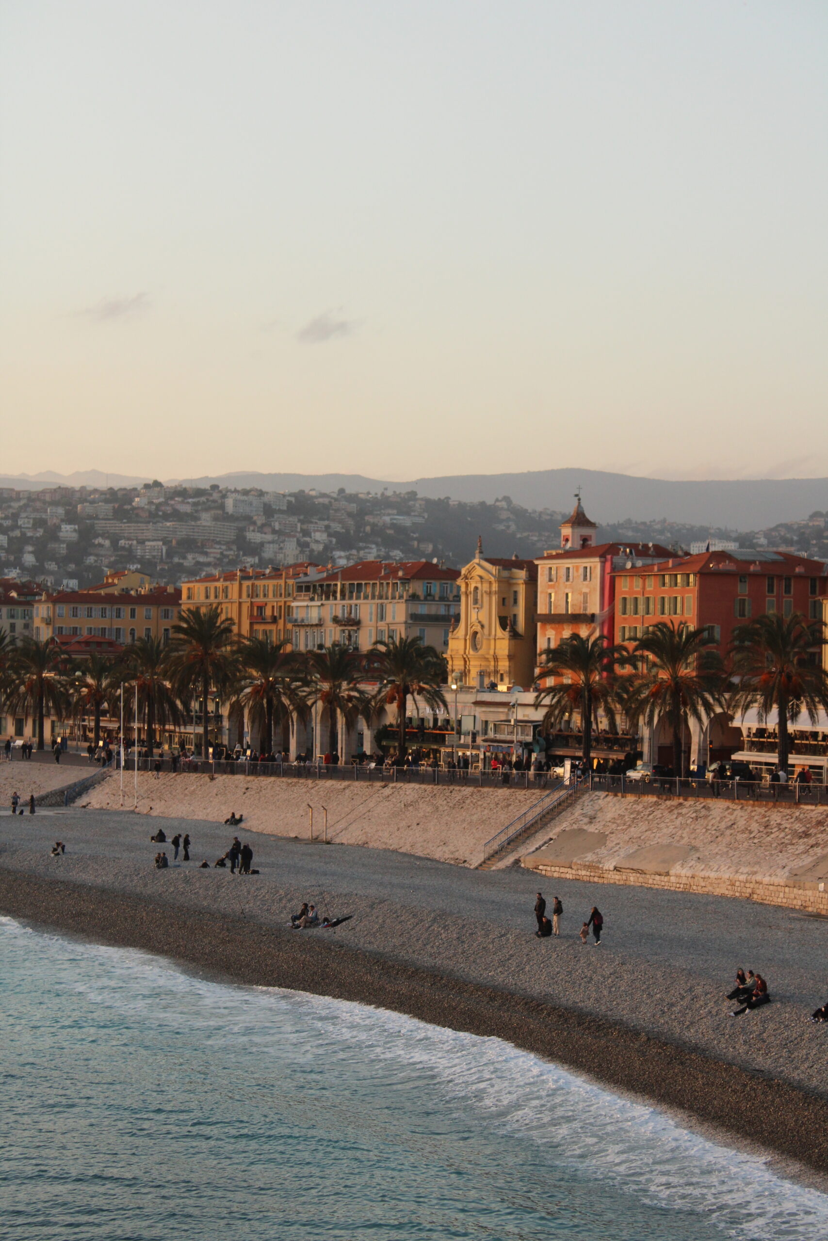 Panoramic view of Nice from Colline du Château, showing terracotta rooftops, the Mediterranean coastline, and the azure sea under a sunny sky.