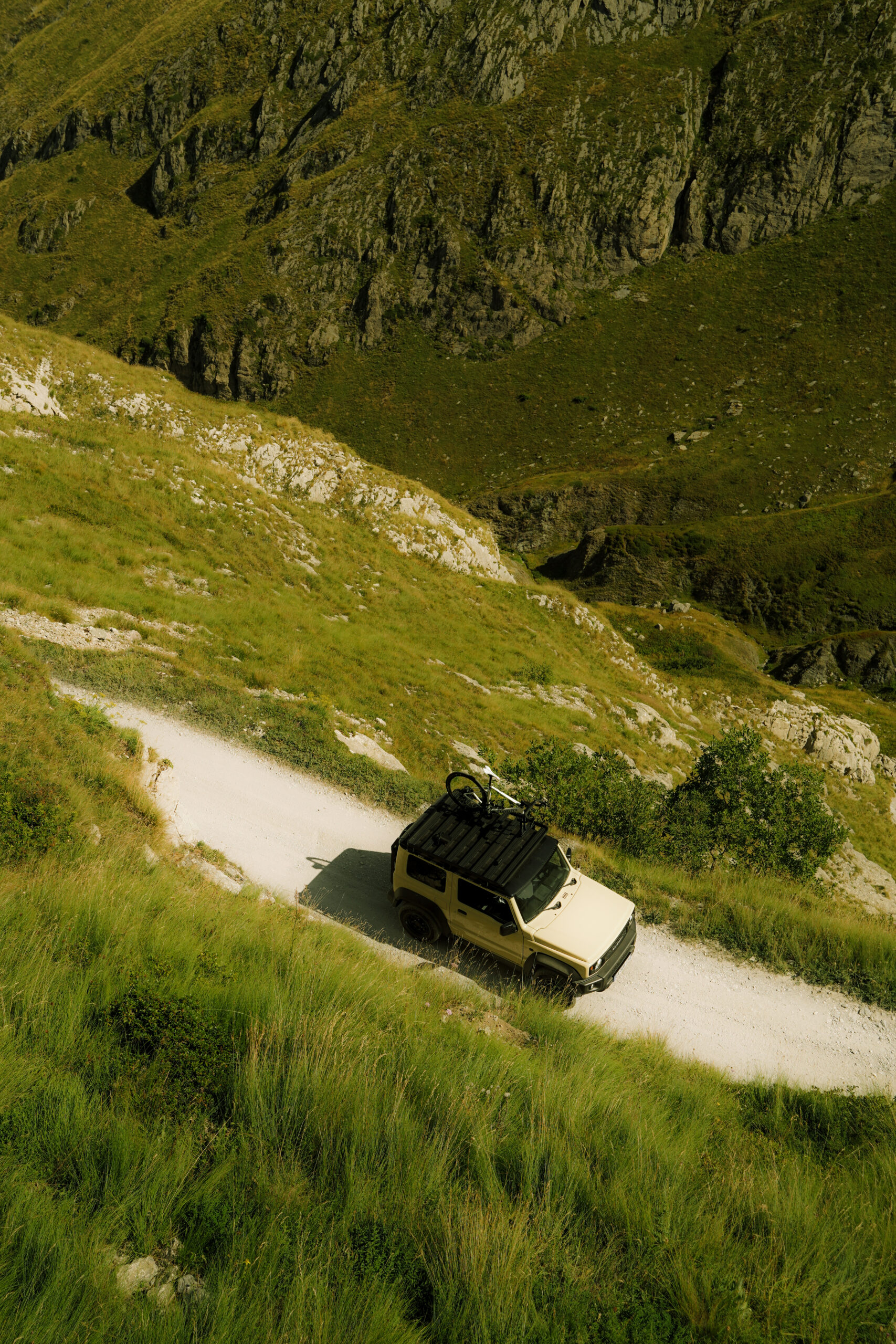 Suzuki Jimny driving the Salt Road Italy 4x4 with mountain views and bikers on the trail